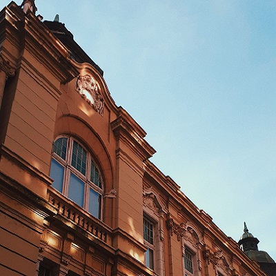 Widok na architekturę budynku z dekoracyjnym detalem, podświetlonym promieniami słońca na tle niebieskiego nieba.