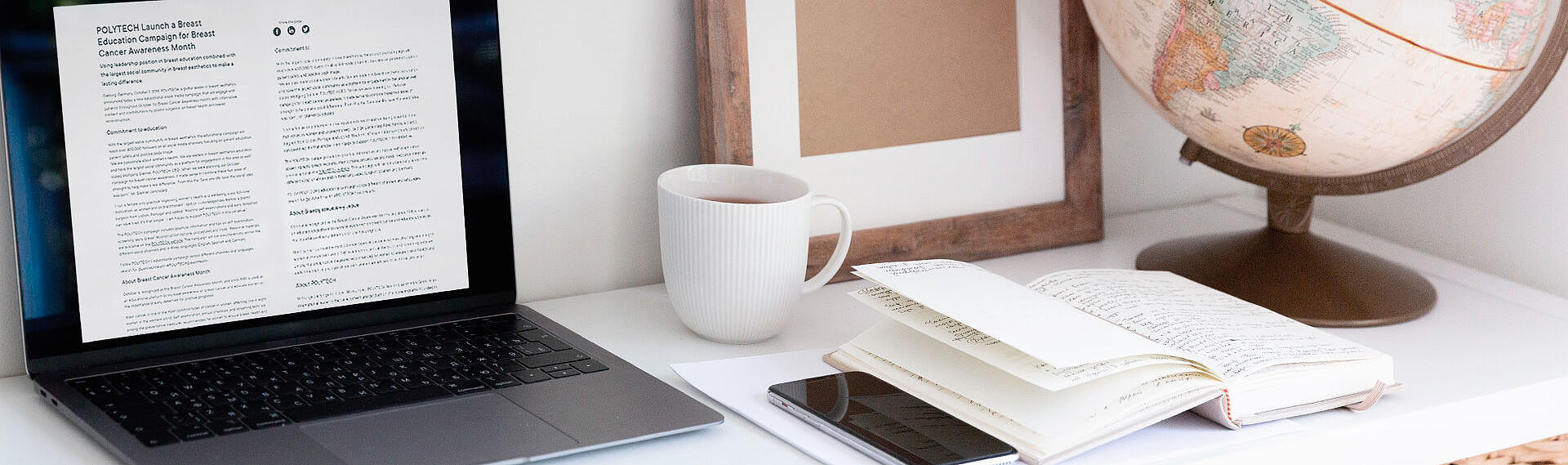 Ein Laptop mit einem geöffneten Dokument, eine Tasse, ein Globus und ein Notizbuch auf einem Schreibtisch.